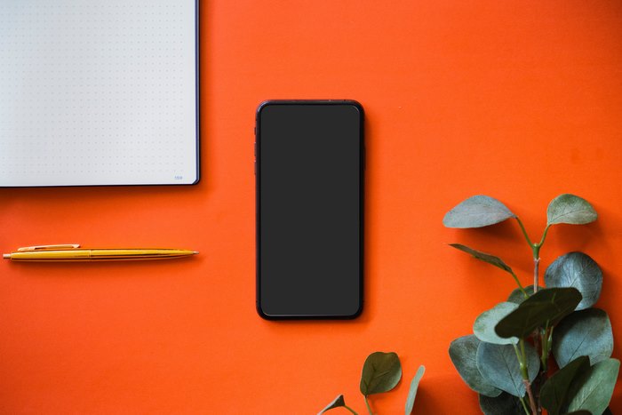 Black iPhone on an orange surface with a notebook and pen