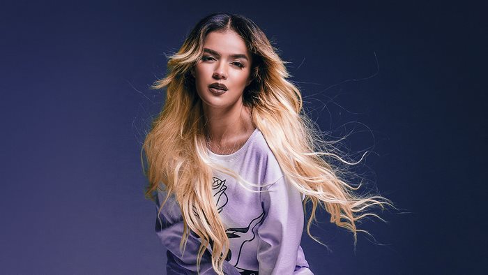 Karol G posing against a dark blue background