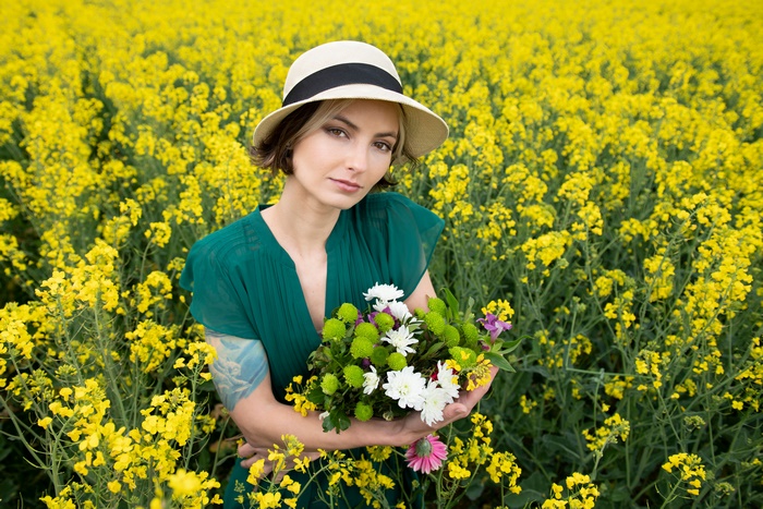 Woman in Hat Holding Flowers in Rapeseed Field