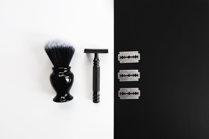 Black shaving brush, razor, and blades on white and black background