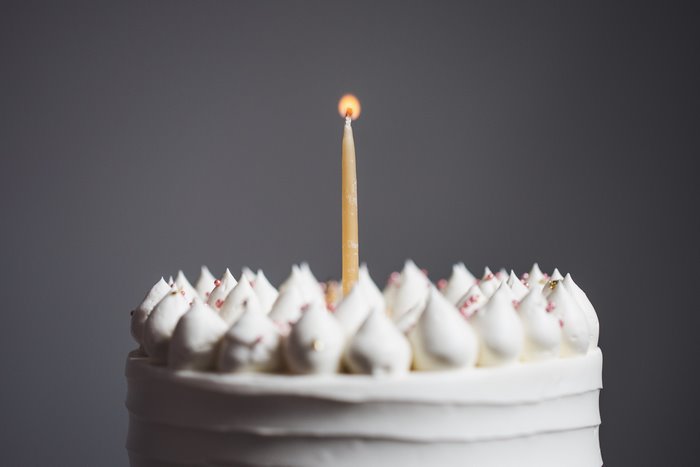 Single lit candle on a white birthday cake