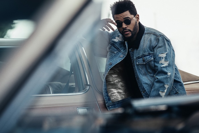 The Weeknd leans on a car wearing a denim jacket