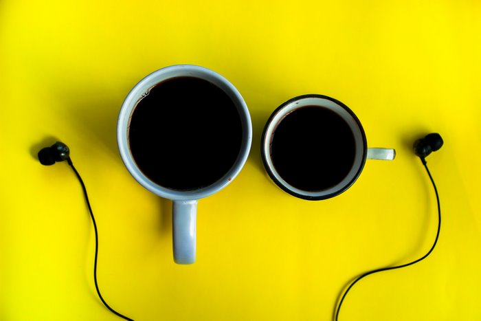 Two cups of coffee and earphones on yellow background