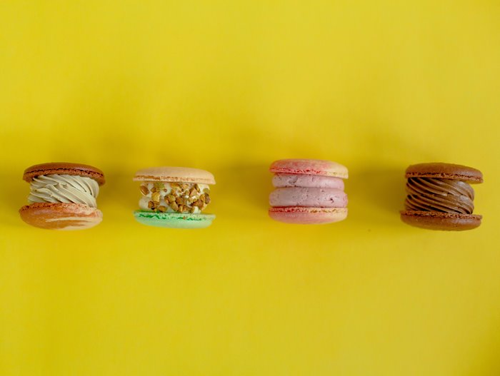 Four colorful macarons on a yellow background