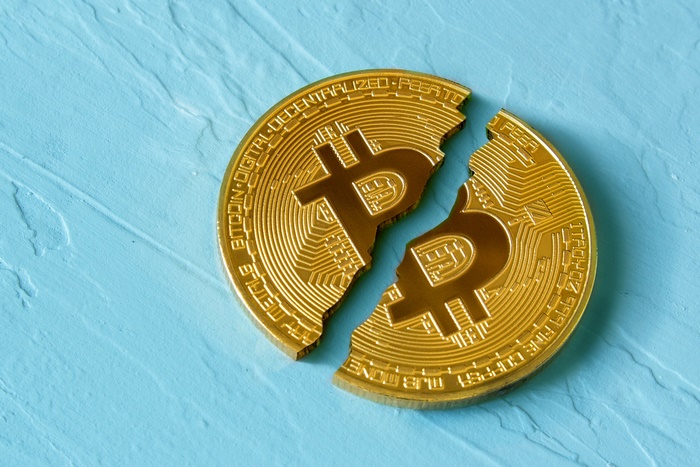 Broken Bitcoin coin on a blue textured surface