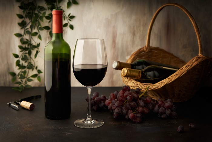 Still life with red wine, grapes, and bottles in a basket