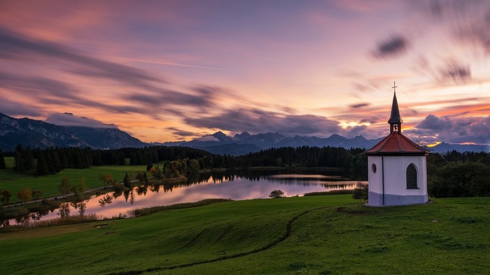 Chapel by a lake at sunset with mountains