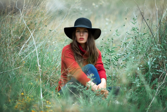 Woman in a hat and red sweater sitting in grass