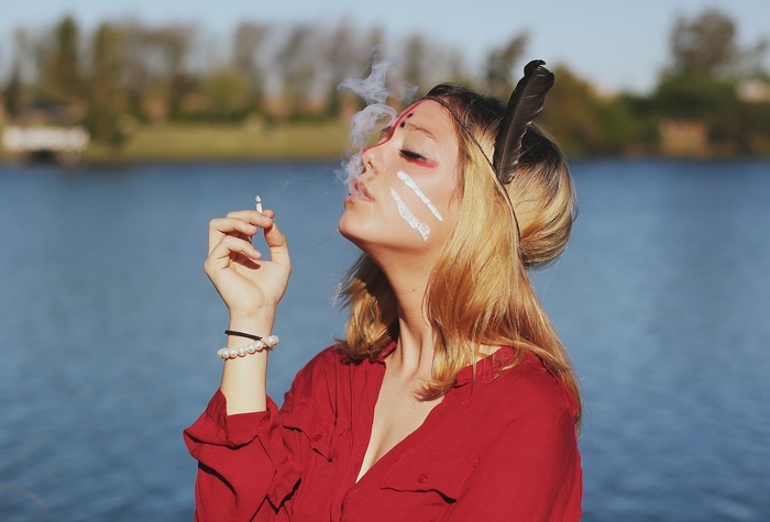 Woman with face paint smoking by a lake