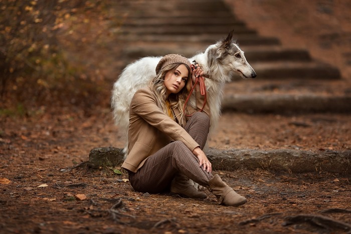Woman and Borzoi dog sitting on forest path