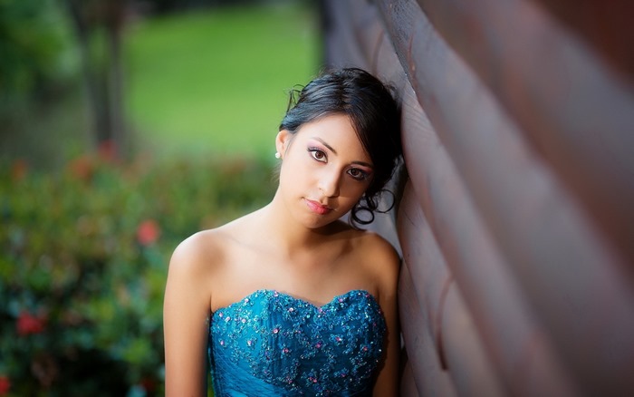 Young woman in a blue dress leaning against a wooden wall