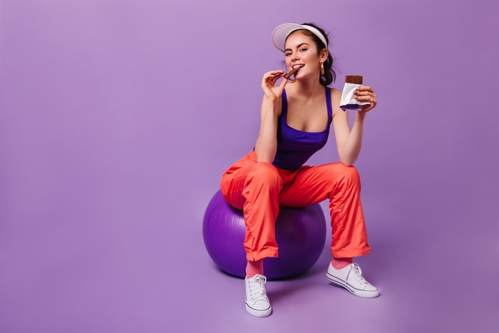 Woman in athletic wear eating chocolate on a yoga ball