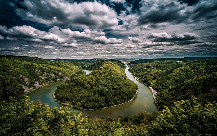 Meandering River Through Green Forest Hills Under Cloudy Sky