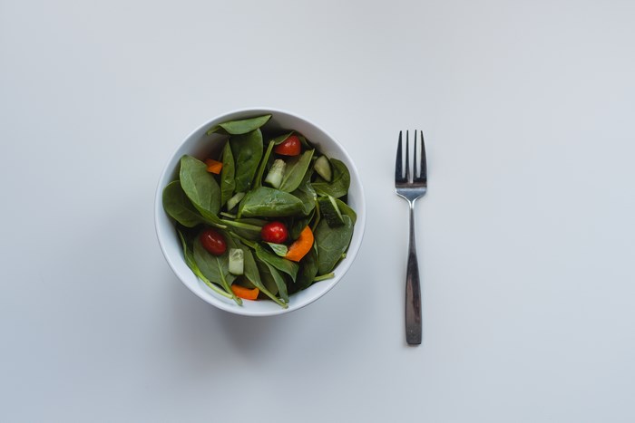 A bowl of green salad with cherry tomatoes and cucumber next to a fork