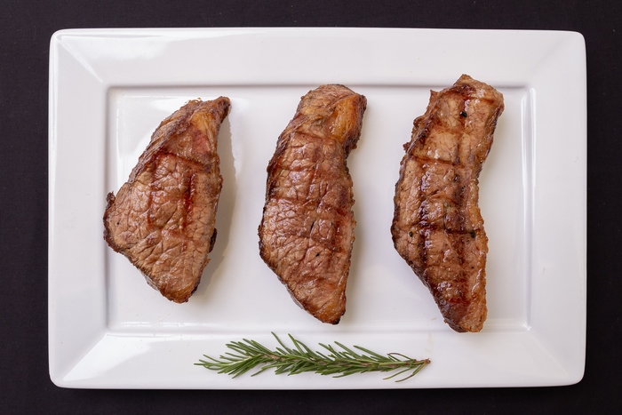 Three grilled steaks on a white plate with rosemary
