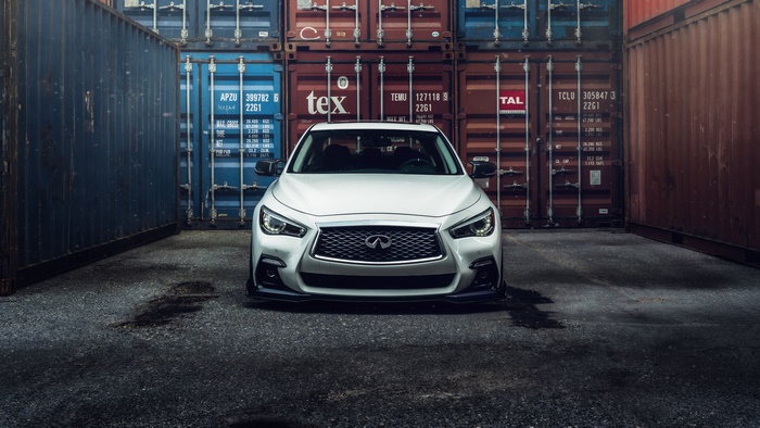 White Infiniti Q50 parked between shipping containers