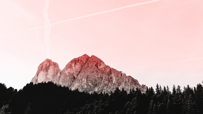 Mountain peaks above a dark forest with pink sky