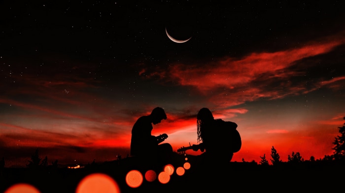 Couple playing guitars under a crescent moon and red sky