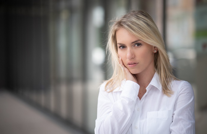 Blonde woman in white shirt with hand on face