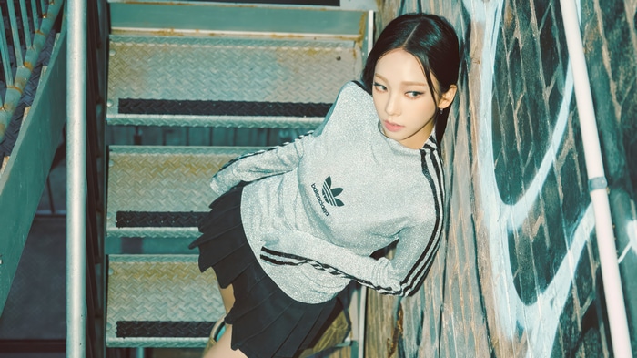 Karina in Adidas outfit leaning against graffiti wall