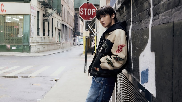 J-Hope leans against a brick wall in an urban alley