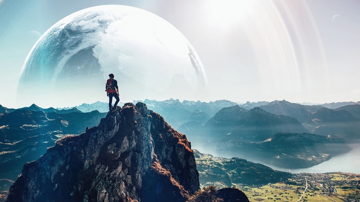 Man on mountain summit with planet and rings in sky