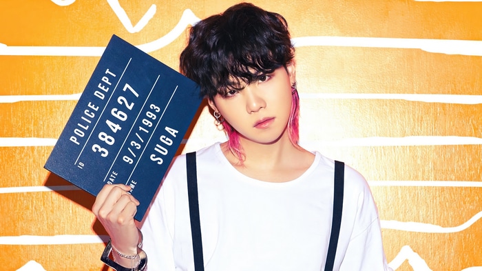 Suga of BTS holding a police mugshot sign