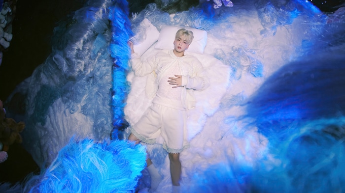 Soobin from TXT lying on a bed of blue and white fluff