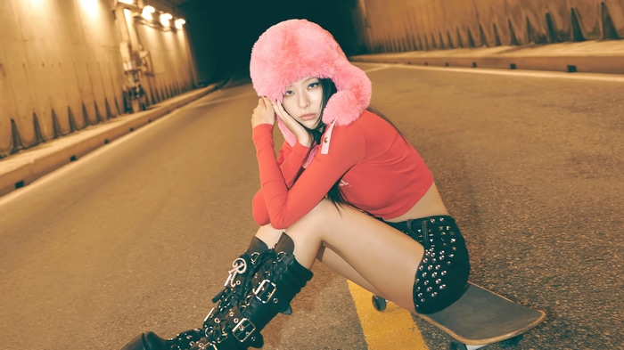 Seulgi in a red top and pink hat on a skateboard