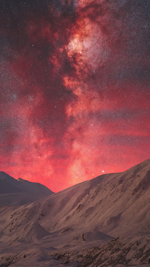 Red Milky Way over snow-covered mountains at night