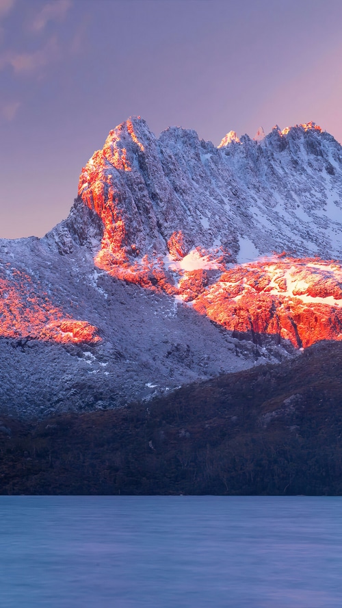 Snow-covered mountain peak at sunrise over a lake