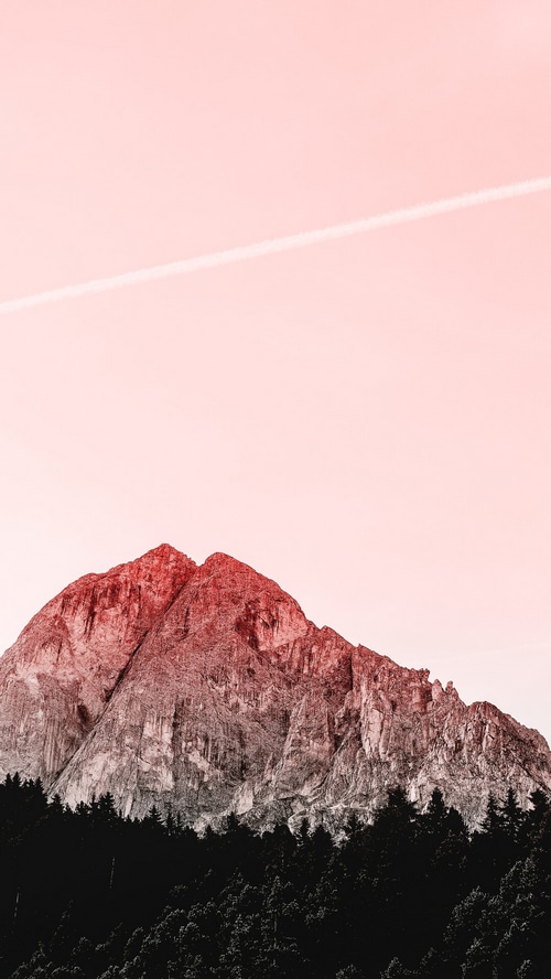 Mountain peak above a dark forest with a contrail