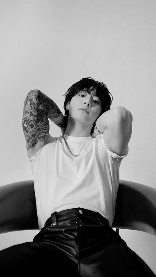 Jungkook with tattoos wearing a white t-shirt and black pants