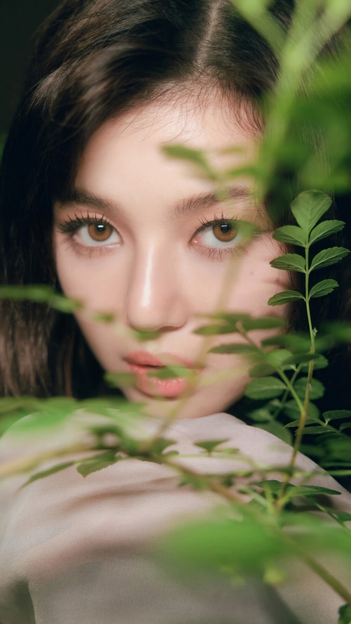 Danielle from NewJeans peeking through green leaves
