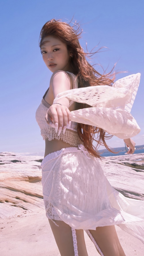 Ningning from Aespa in a white outfit on a rocky shore