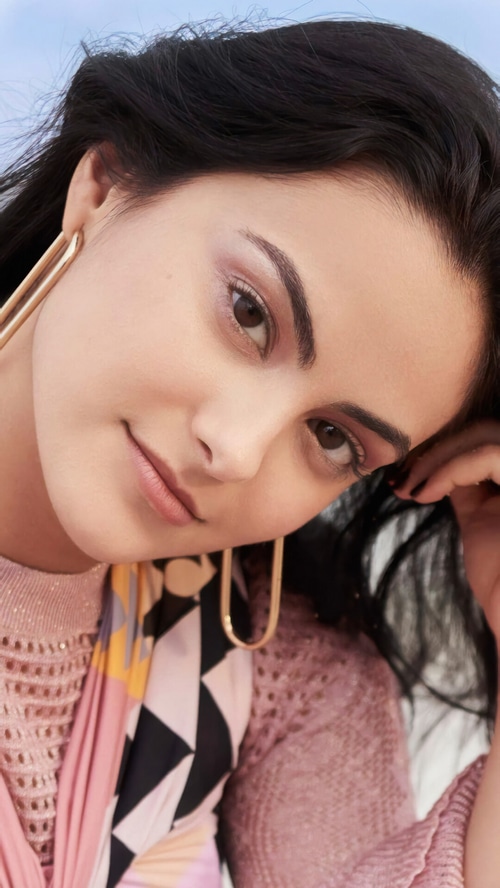 Camila Mendes wearing pink sweater and gold earrings