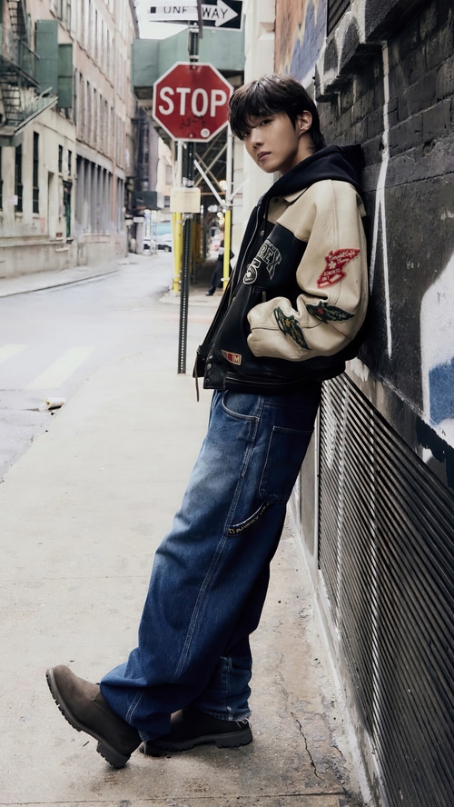 J-Hope leans against a brick wall in a city alley