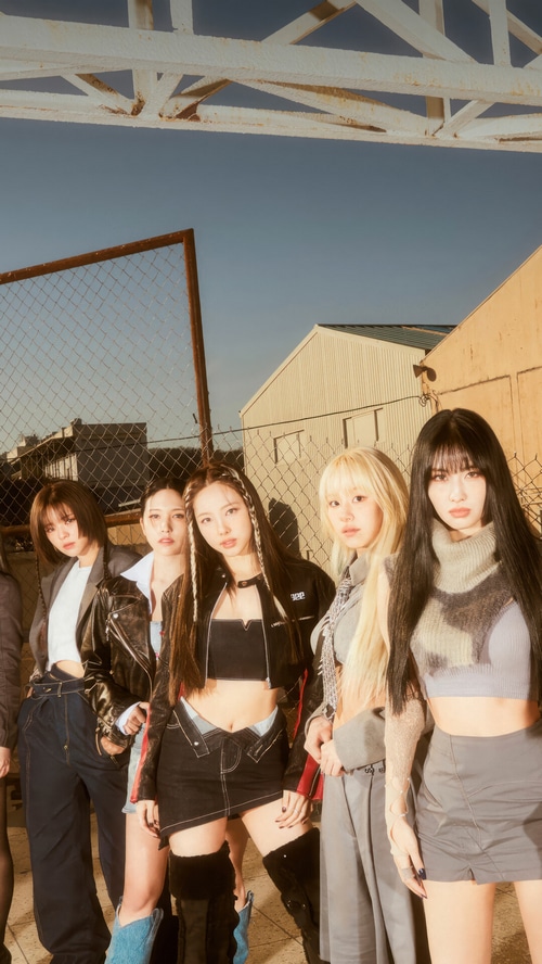 TWICE members posing in an outdoor industrial setting