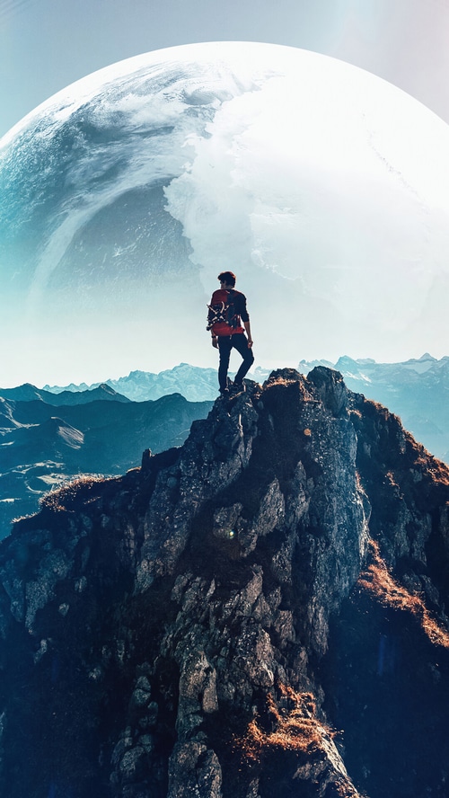 Man on mountain peak with large planet in sky