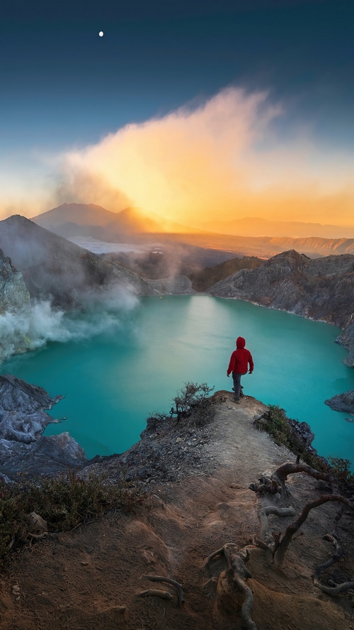 Person overlooking Ijen volcano crater lake at sunrise