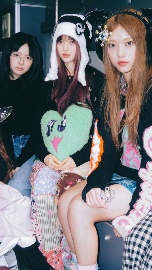 NewJeans members posing with a heart pillow