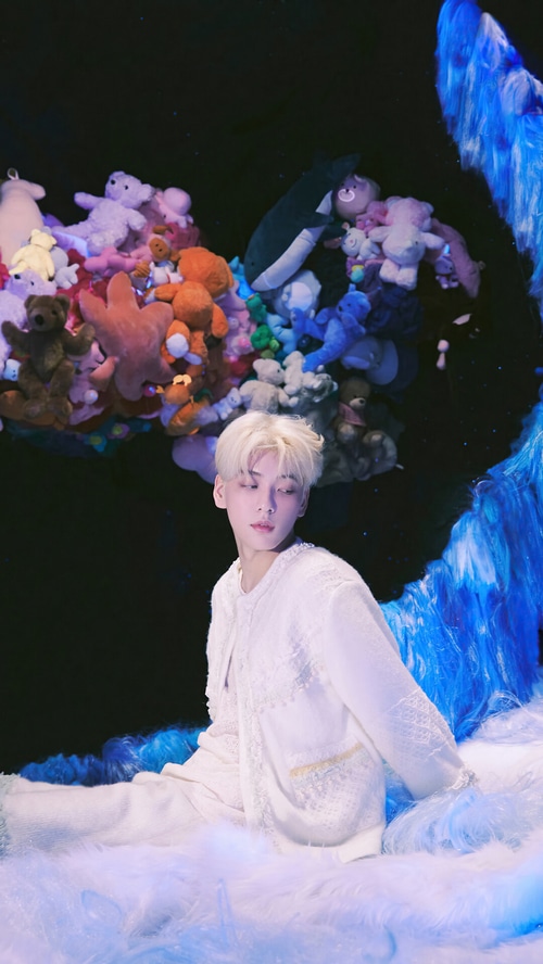 Soobin from TXT in white outfit surrounded by plush toys