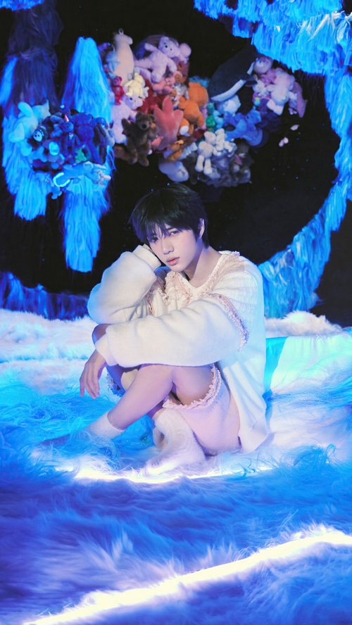 Beomgyu from TXT sitting on a fluffy blue surface