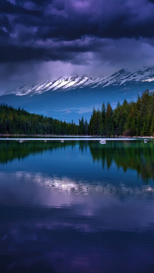 Snow-capped mountains reflected in a calm lake with pine trees