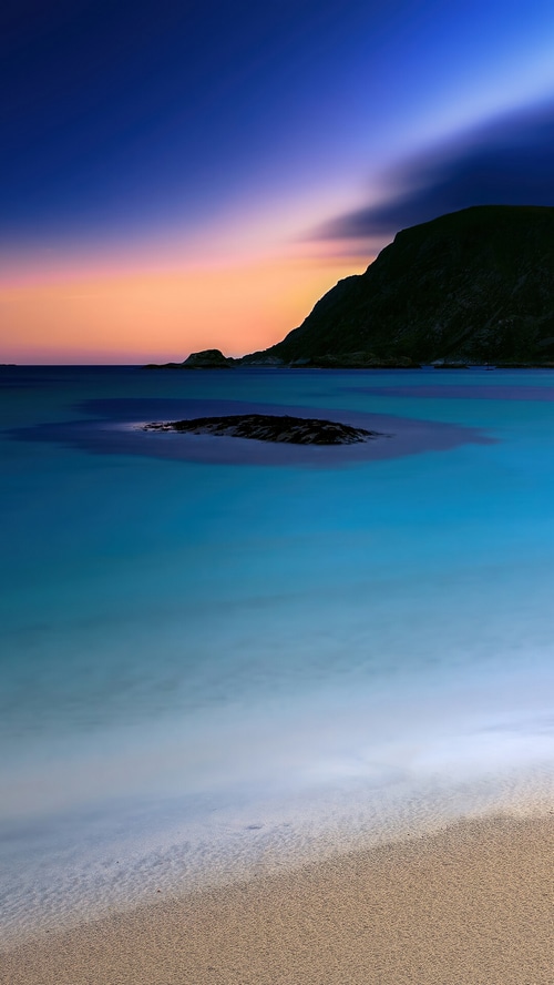 Beach sunset scenery with calm ocean and dark mountain