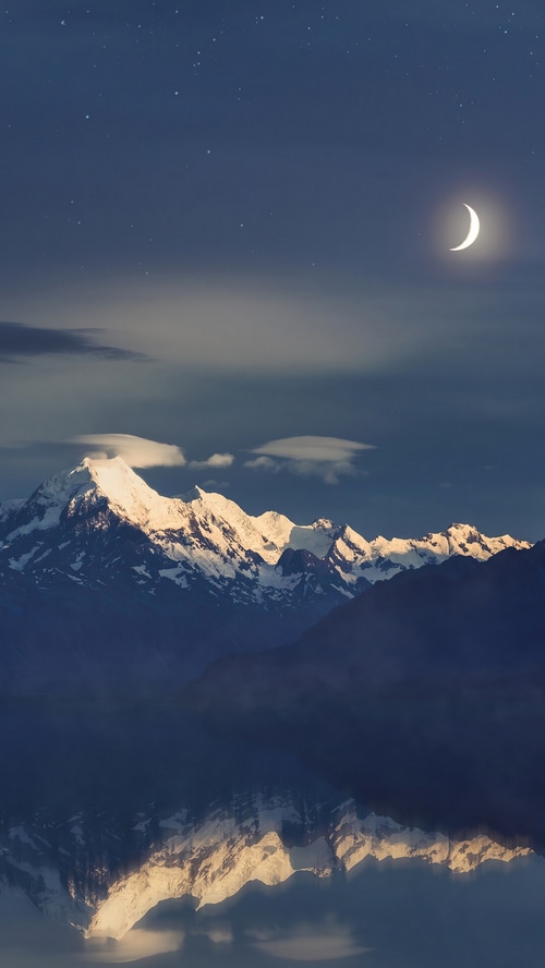 Snowy mountains under a crescent moon and stars