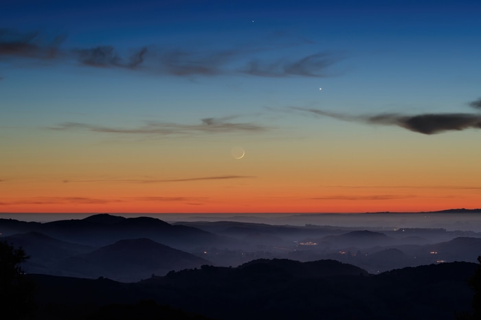 Crescent moon and planets over rolling hills at sunset
