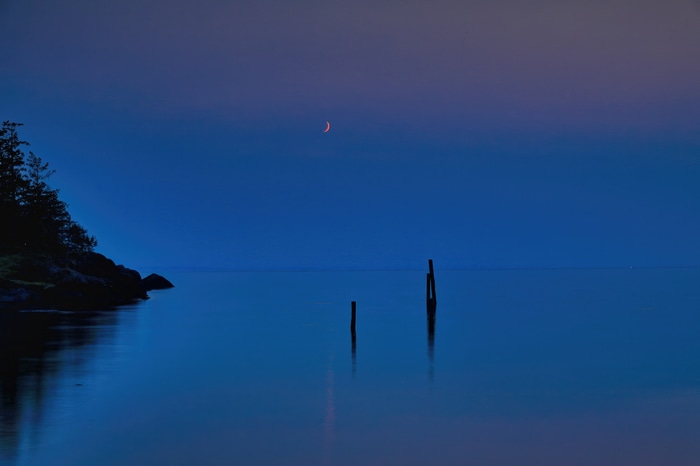 Crescent moon over calm water at dusk