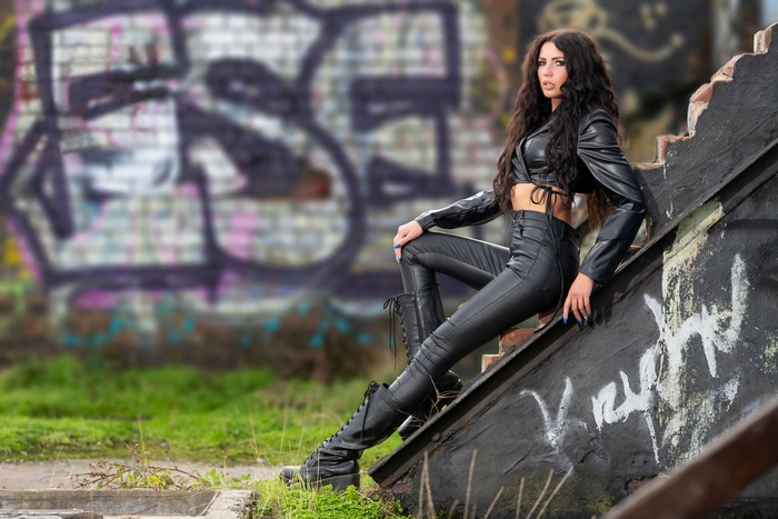 Model in black leather outfit posing on stairs with graffiti