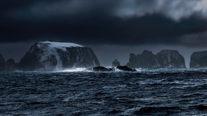 Dark ocean waves crash against rocky islands under a stormy sky
